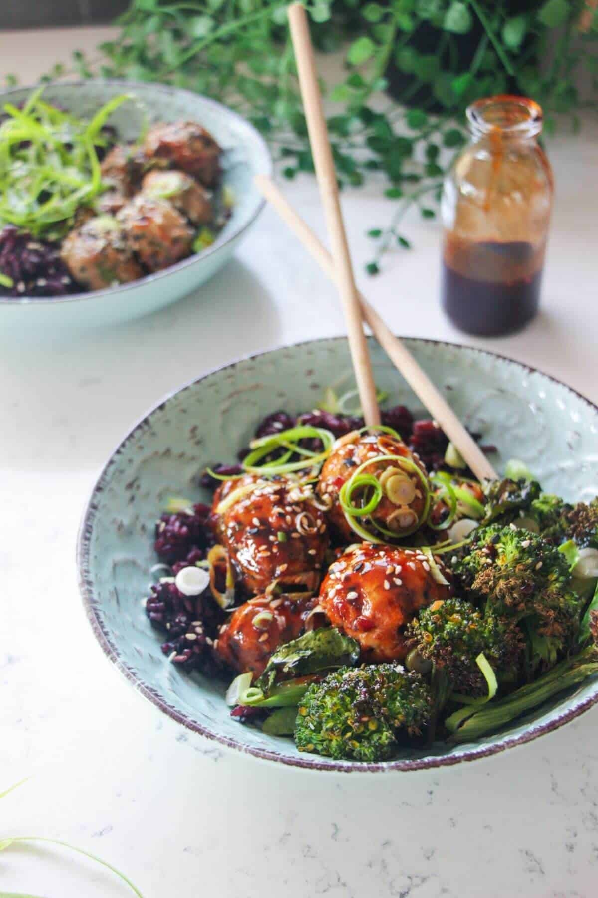 Glazed Asian chicken meatballs with rice and broccoli in a small blue bowl.