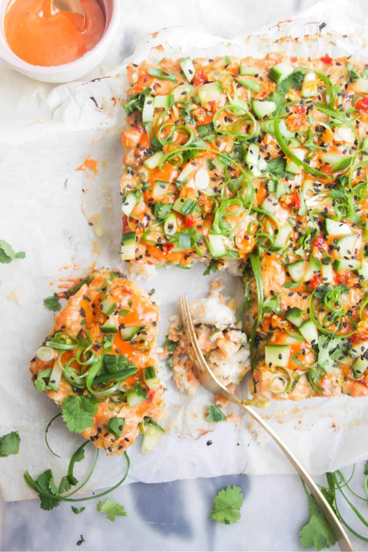 Salmon sushi bake on a grey marble background, with a gold spoon.