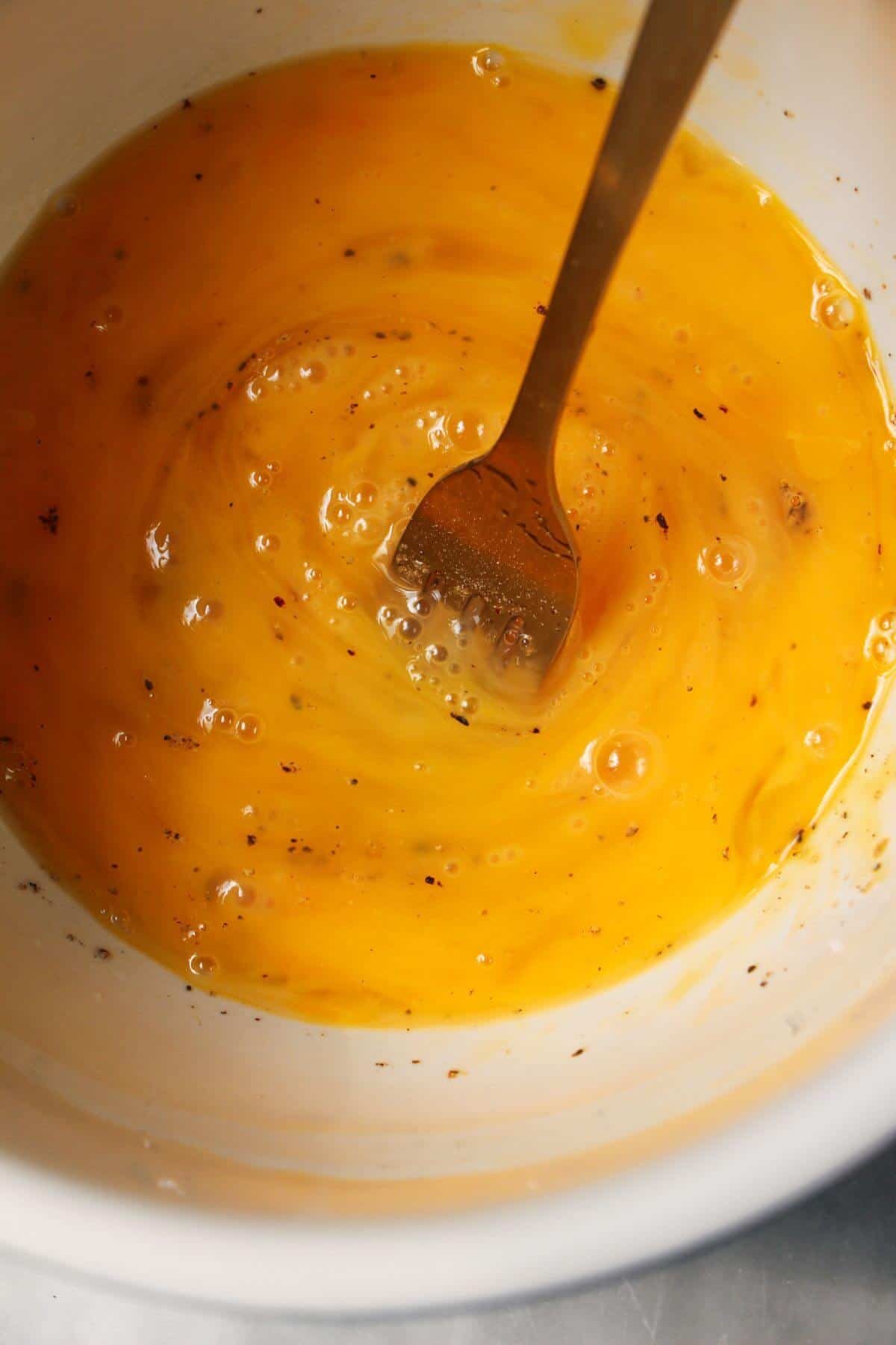 A fork whisking eggs in a small white bowl.