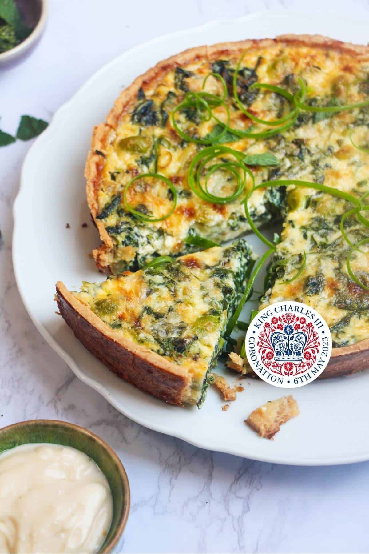 Coronation quiche on a scalloped white plate with a piece cut out of it.