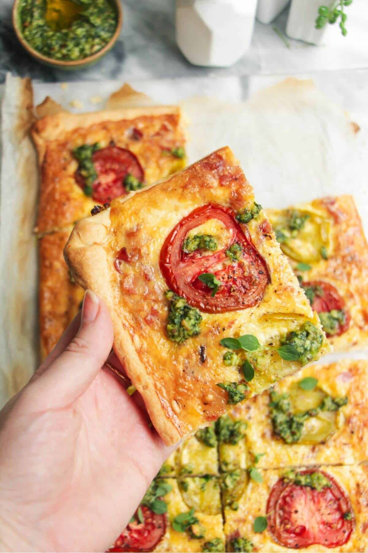 Hand holding up a piece of bacon and egg pie with more pie in the background.
