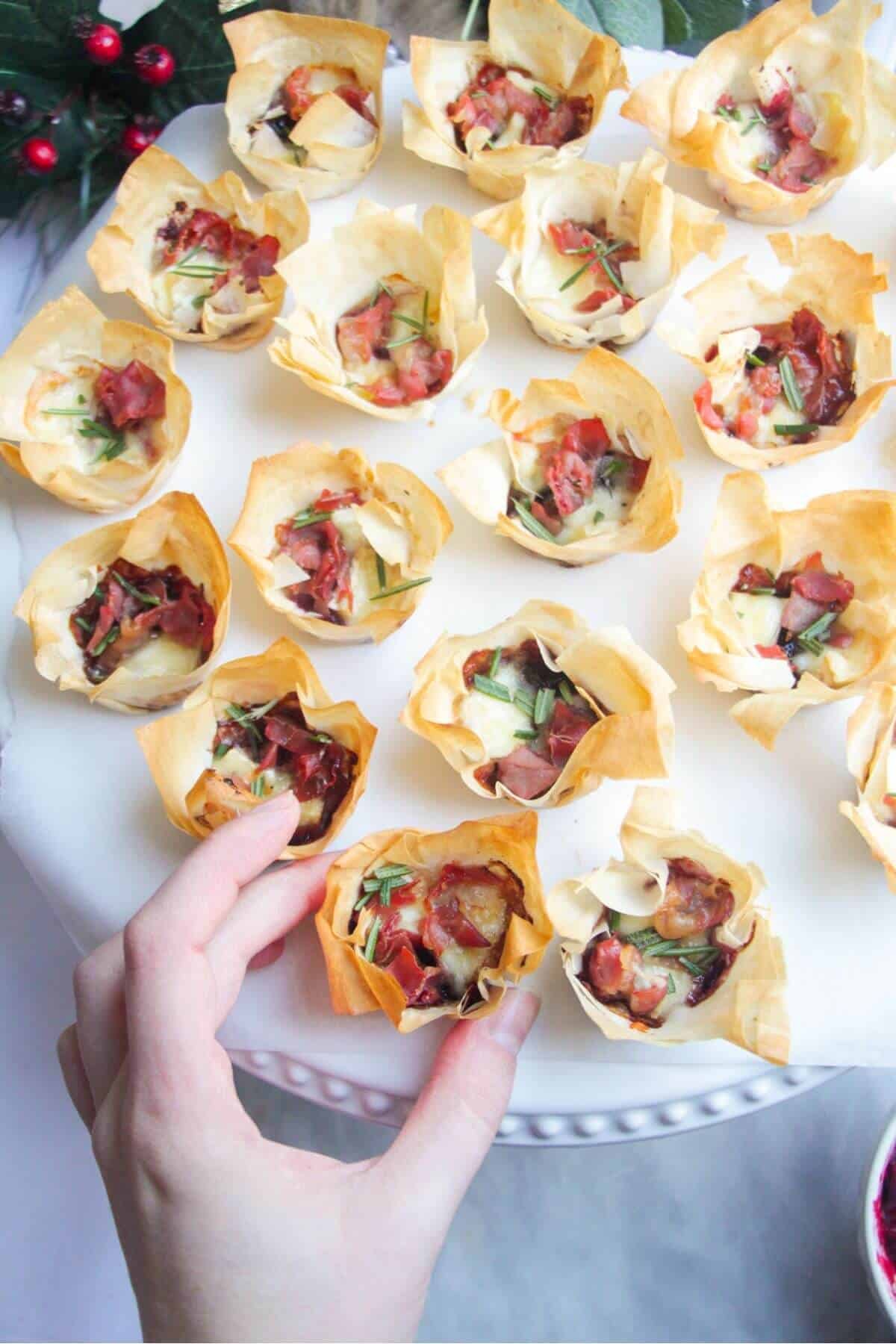 Hand picking up a filo bite with more filo bites on a white plate in the background.