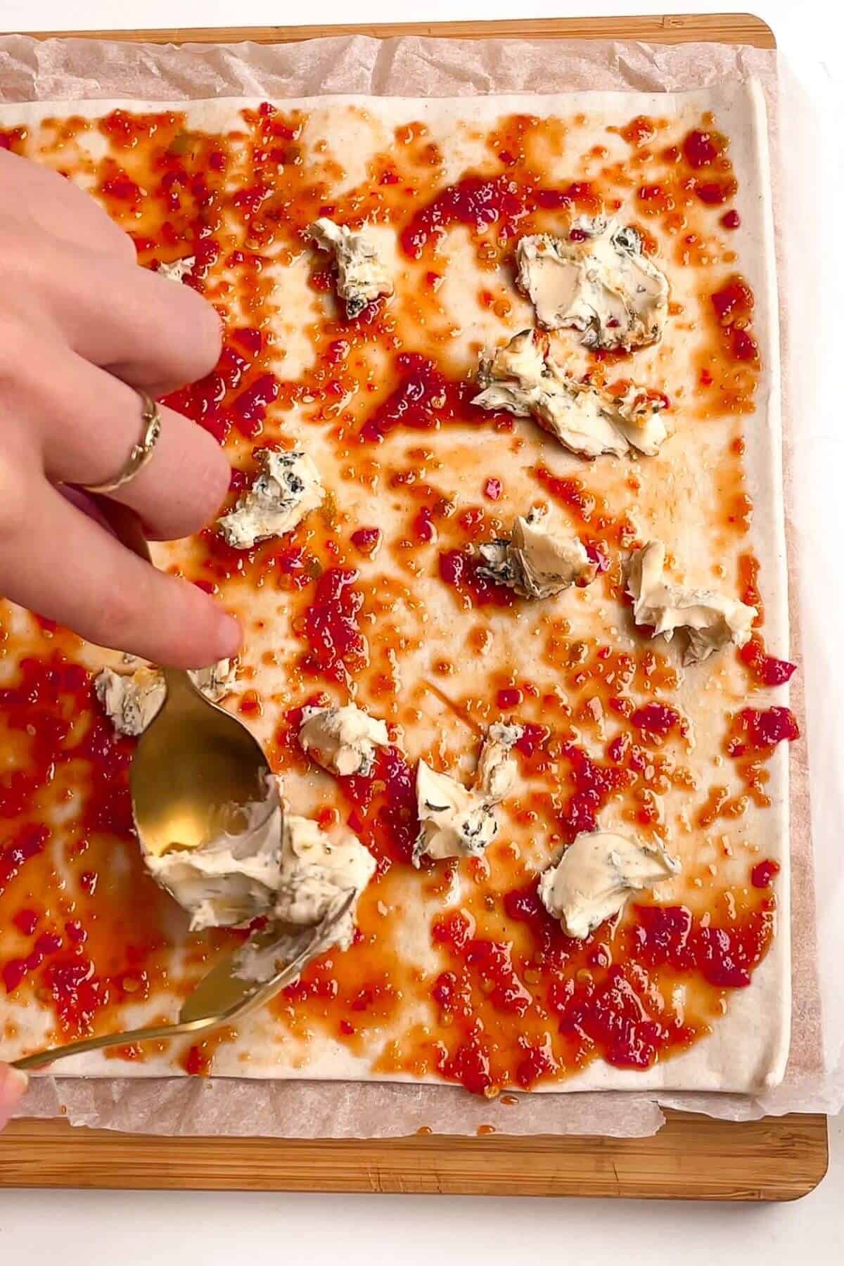Spooning creamy blue cheese onto sweet chilli on puff pastry.