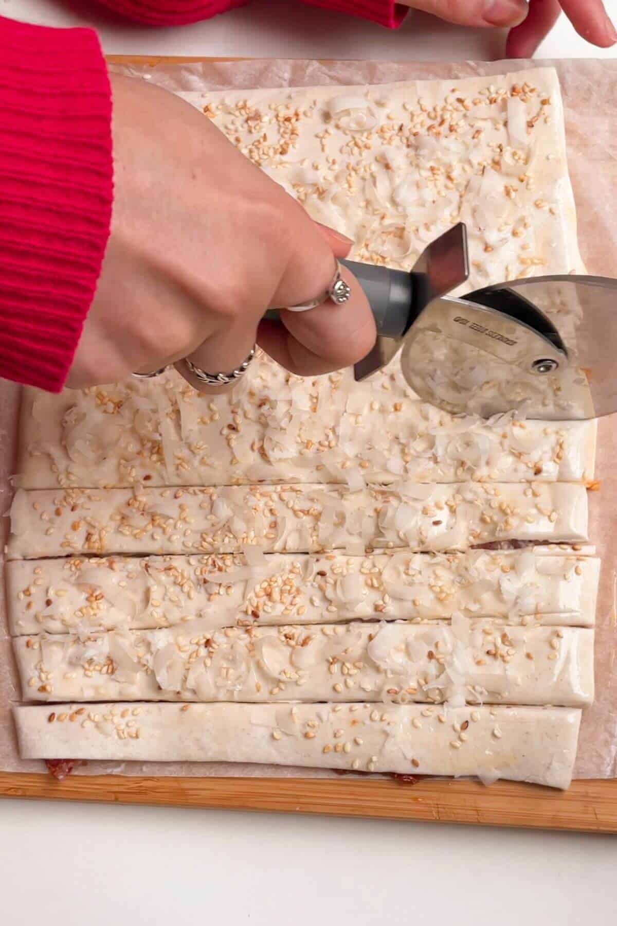 Hand holding pizza cutter, slicing through puff pastry.
