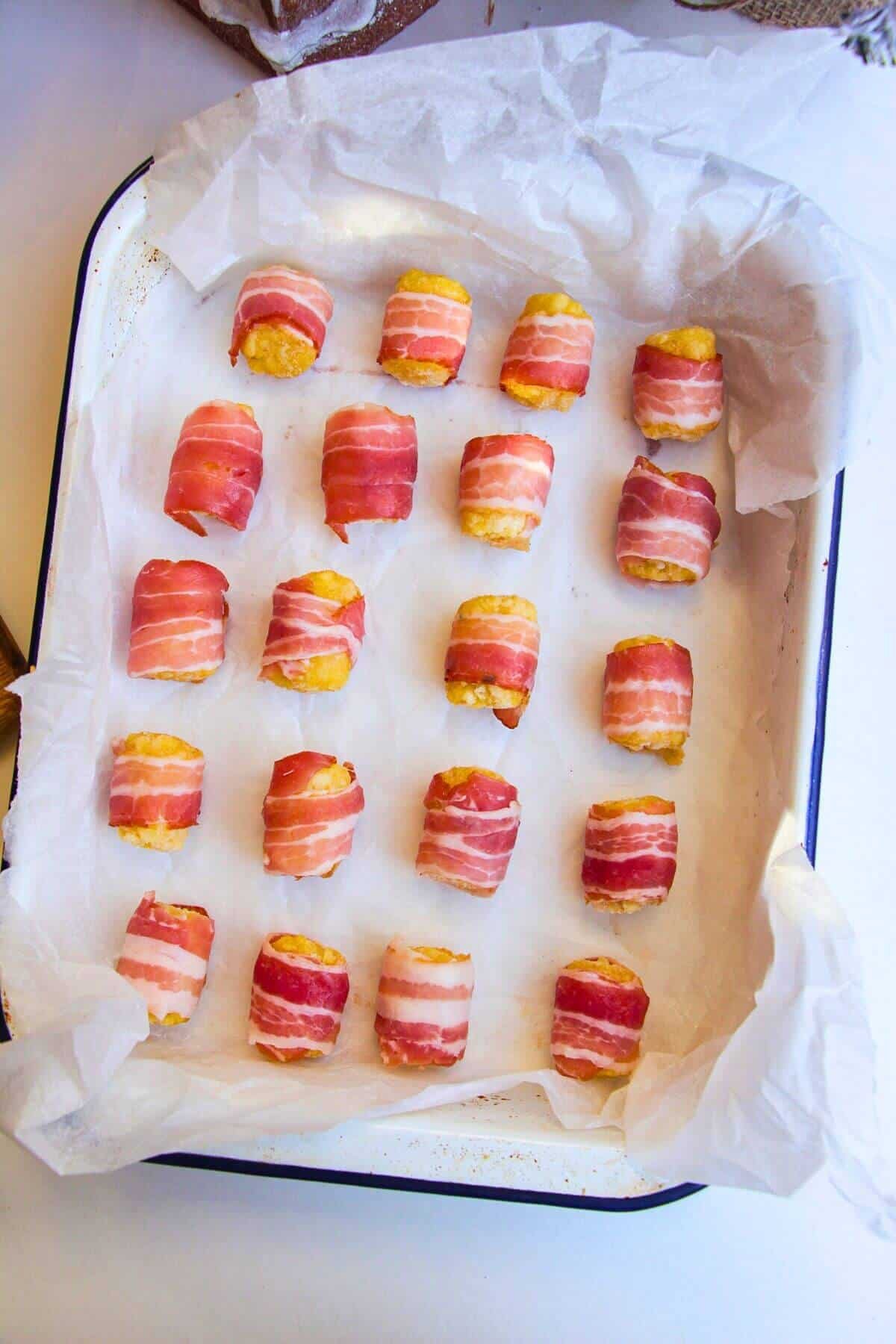 Bacon wrapped around tater tots in an oven dish.