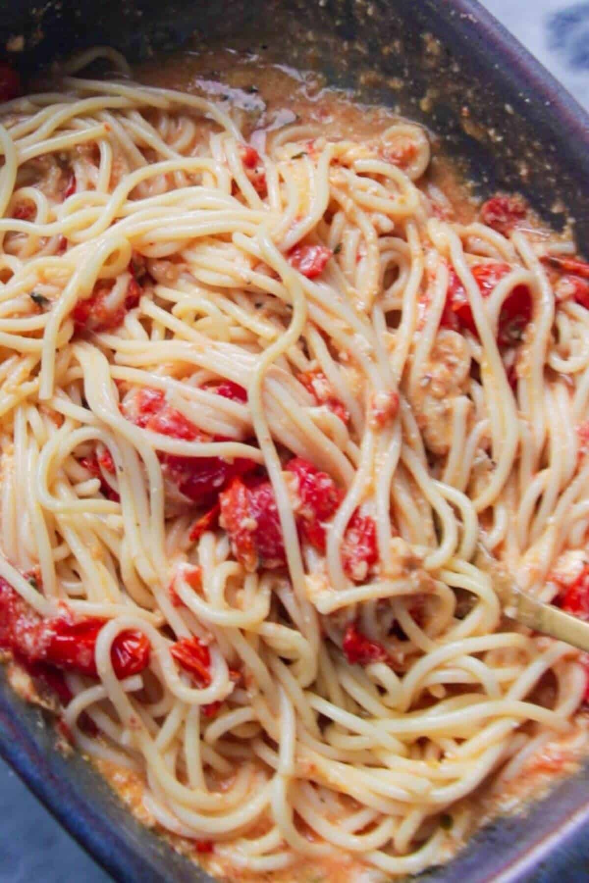 Baked burrata and tomato pasta mixed in a blue oven dish.