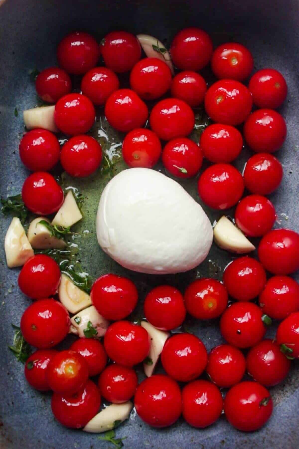 Burrata, cherry tomatoes, garlic and herbs in a small blue oven dish.