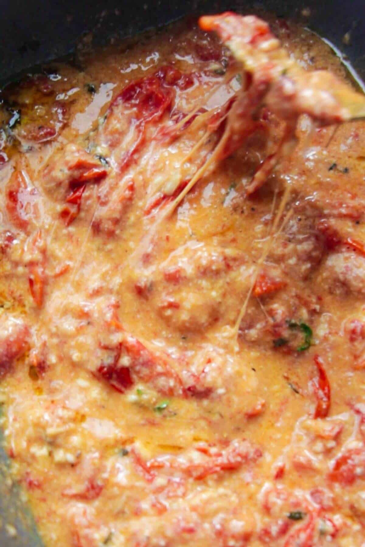 Fork mixing roasted tomatoes, garlic, burrata into a sauce.