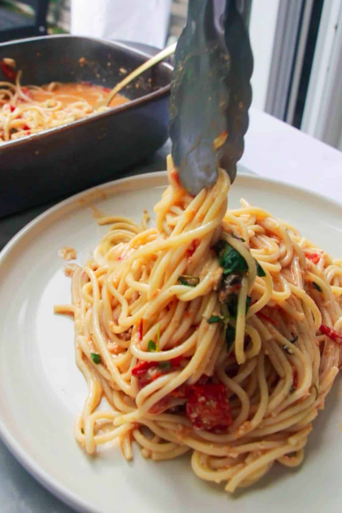 Pasta being transferred to a plate with silver tongs.
