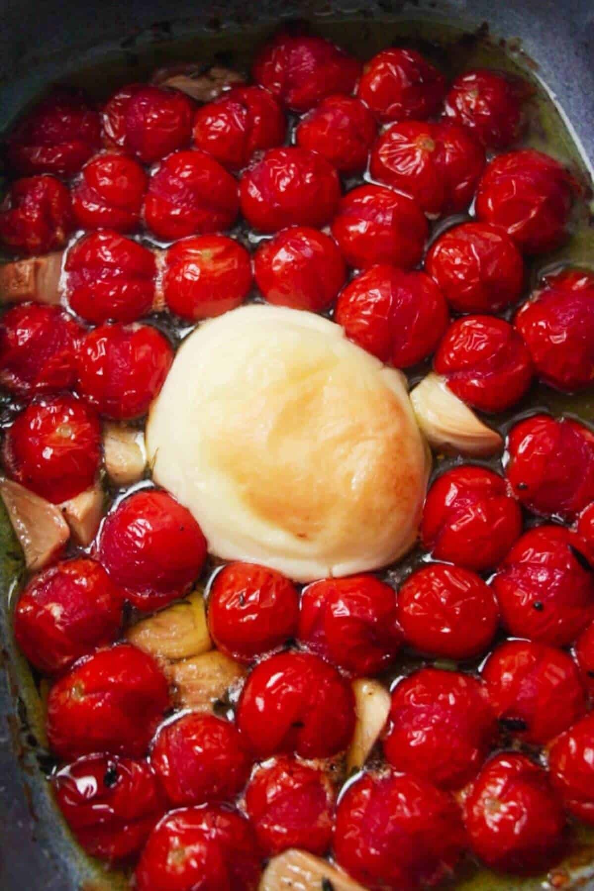 Baked burrata, tomatoes, garlic in a blue dish.
