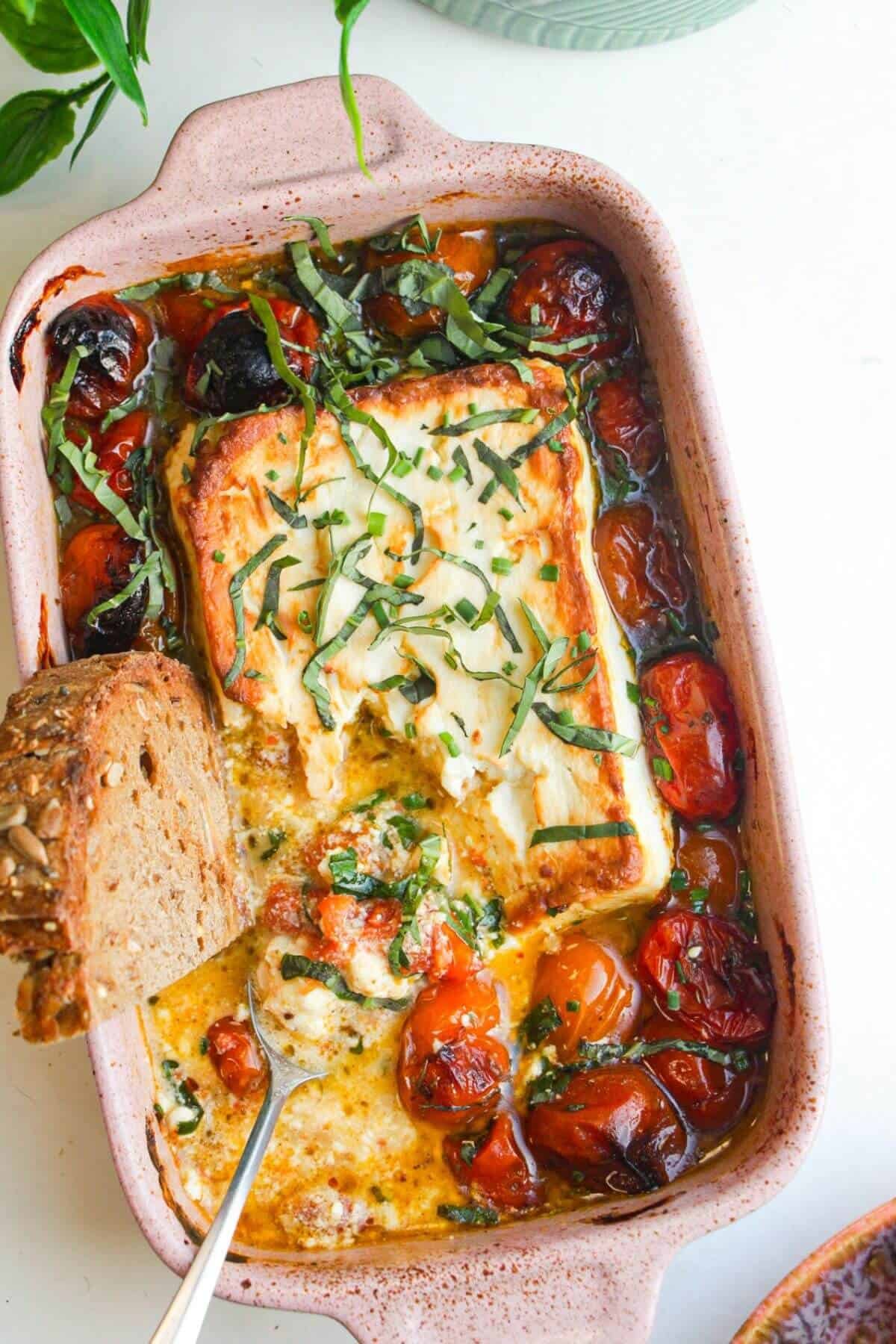 Baked feta and tomatoes in an oven dish with a piece of bread.