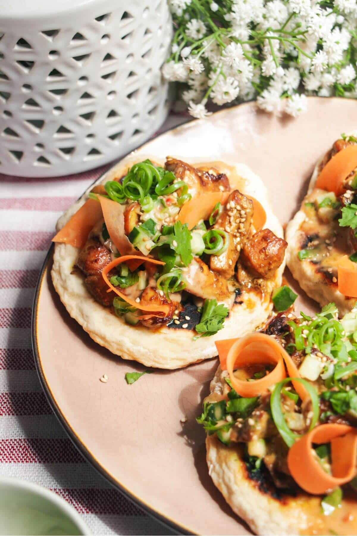 Side view of chicken satay flatbread on a plate.