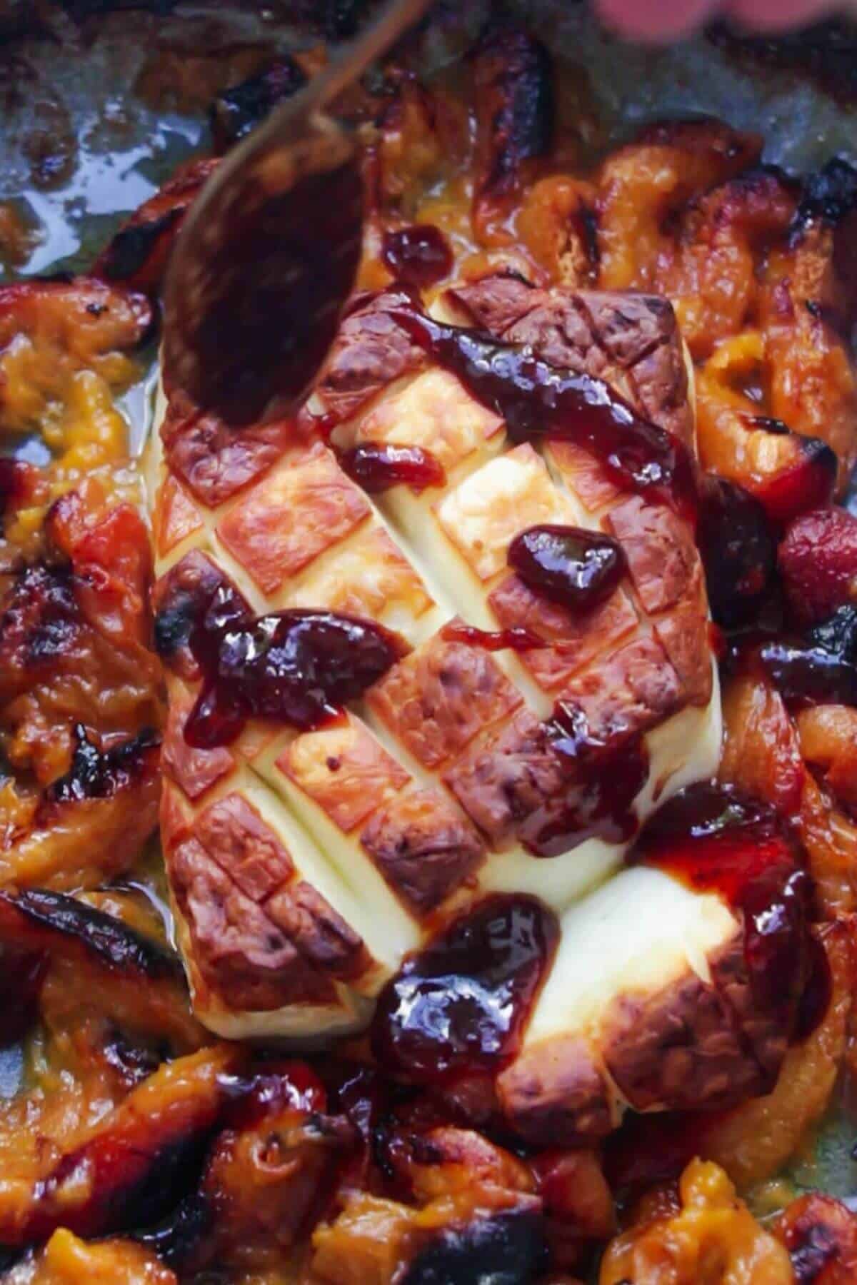 Honey harissa lemon sauce being drizzled on top of baked whole halloumi in a blue oven dish.