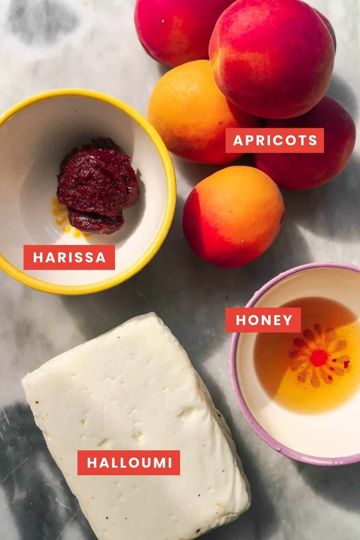 Ingredients for baked whole halloumi laid out on a grey marble background and labelled.