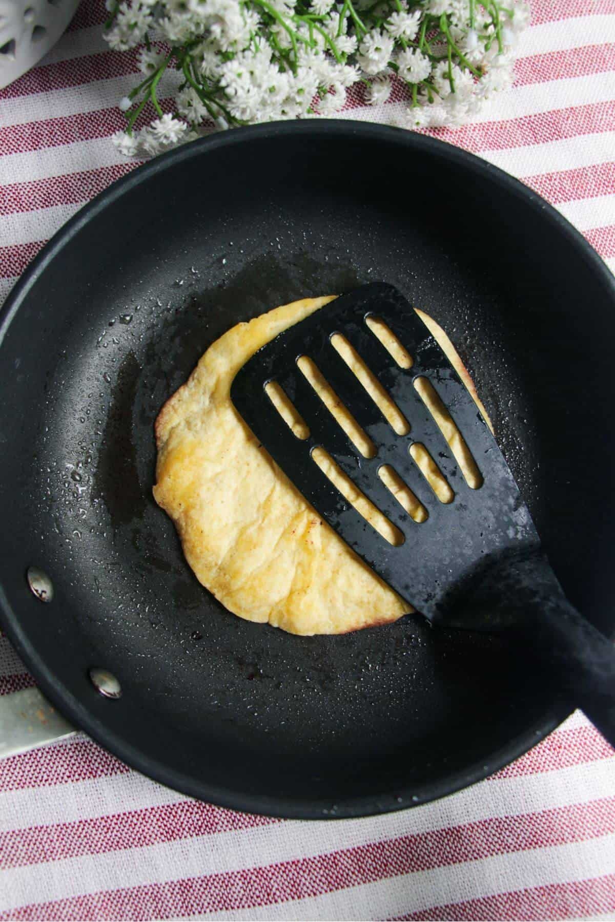 Fish slice pressing mini tortilla into small black pan.