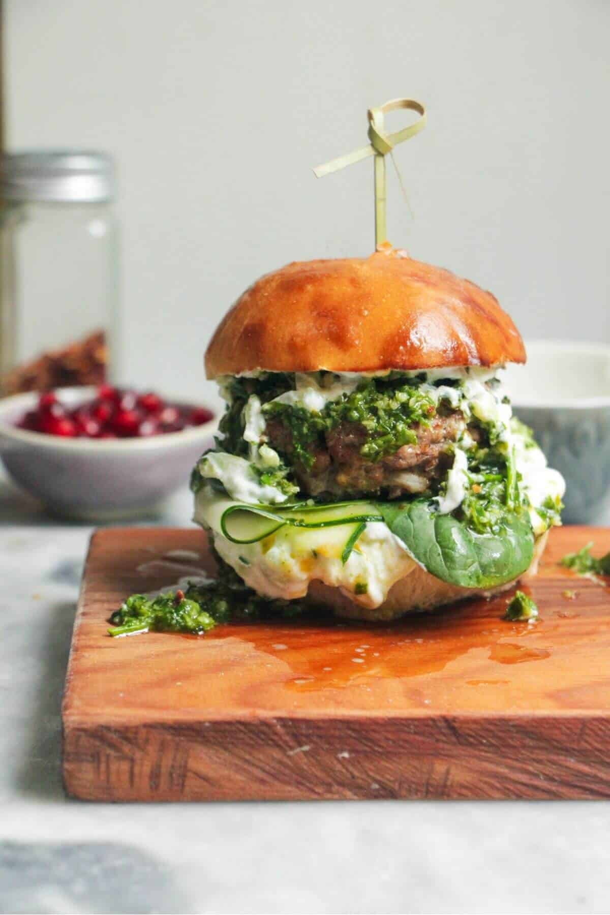 Juicy Greek lamb burger on a small wooden board with a skewer through the top.