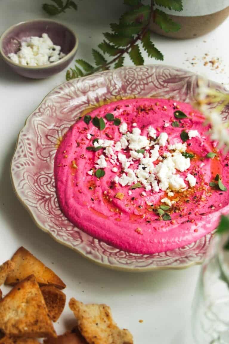 Bright pink beet feta dip on a pink plate with feta crumbled on top and pita chips on the side.