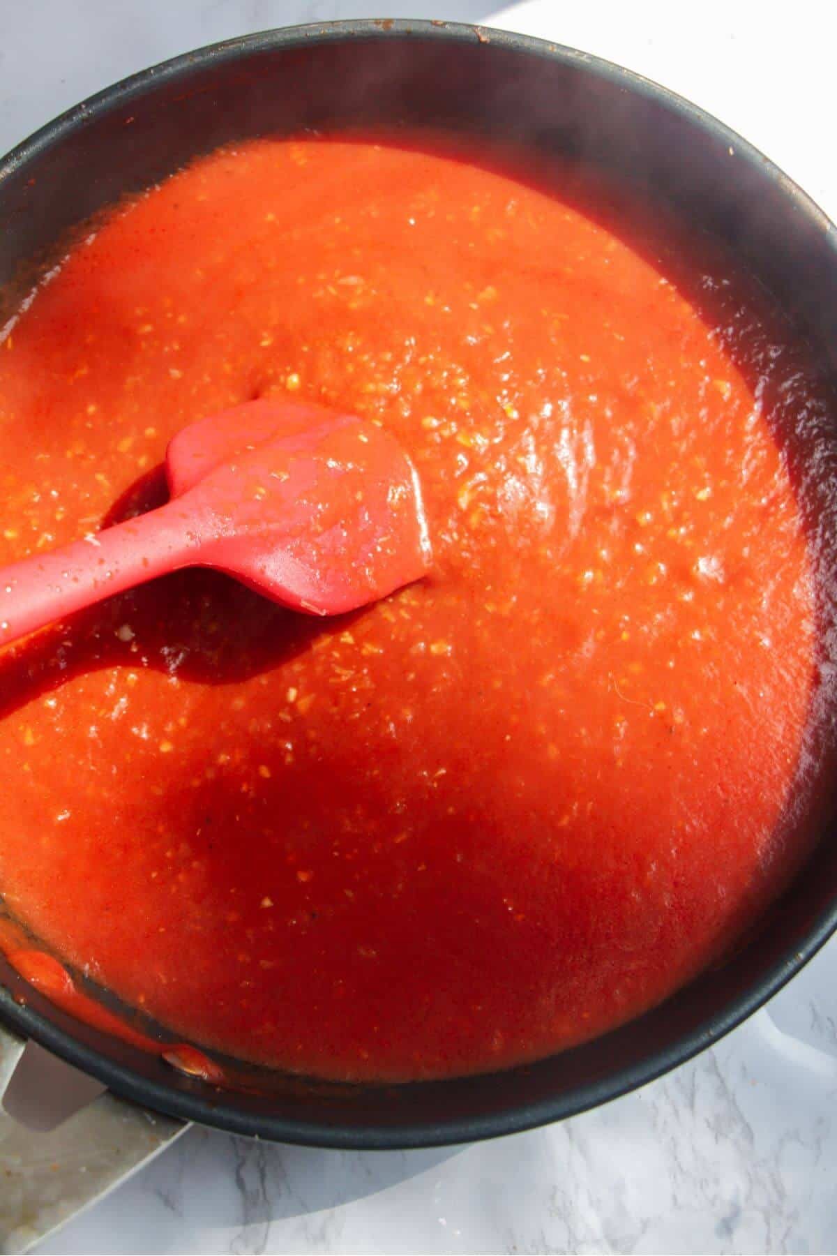 Red spatula stirring thickened bloody mary pasta sauce.