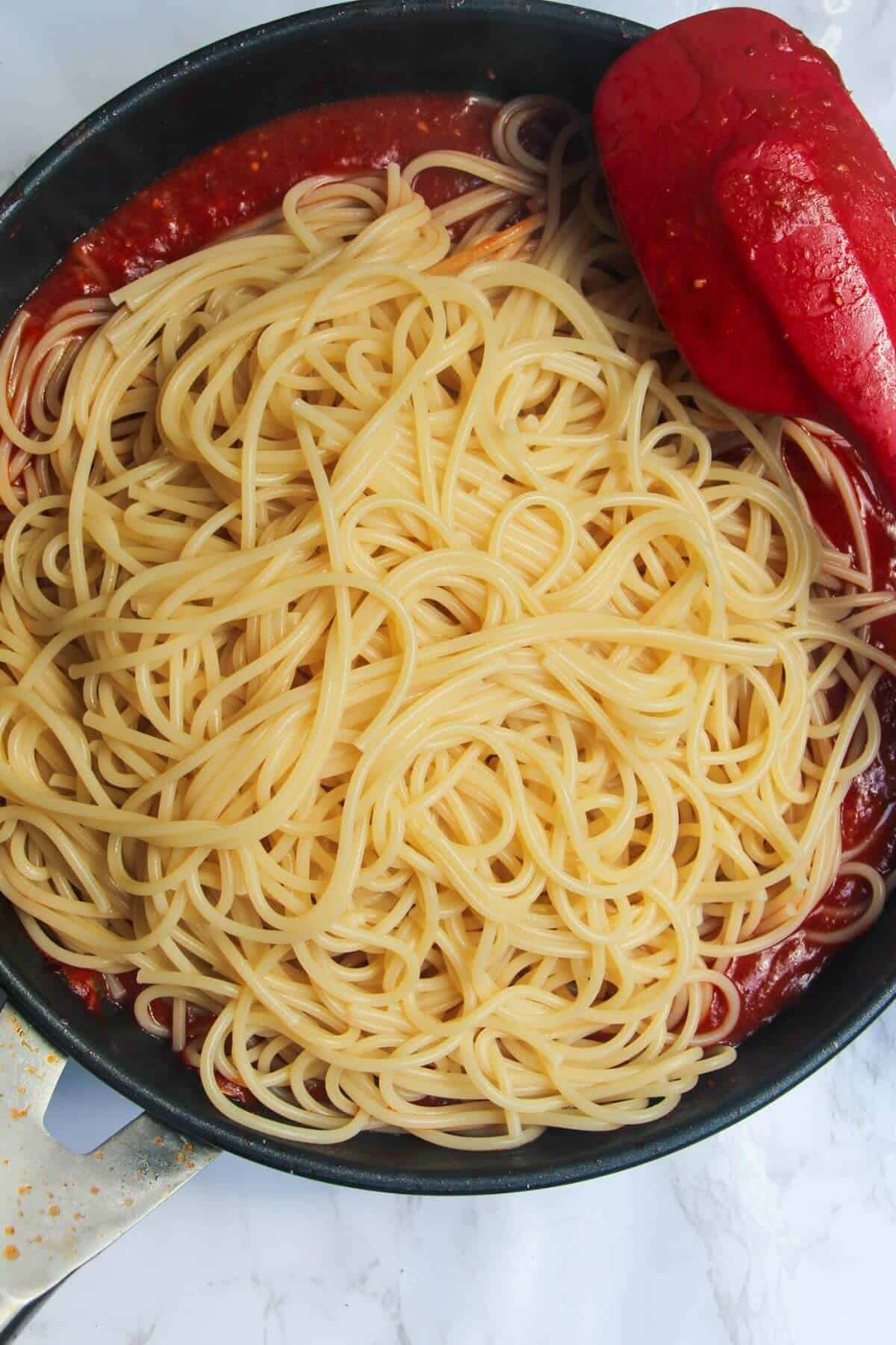 Cooked spaghetti added to bloody mary pasta sauce in a small frying pan.