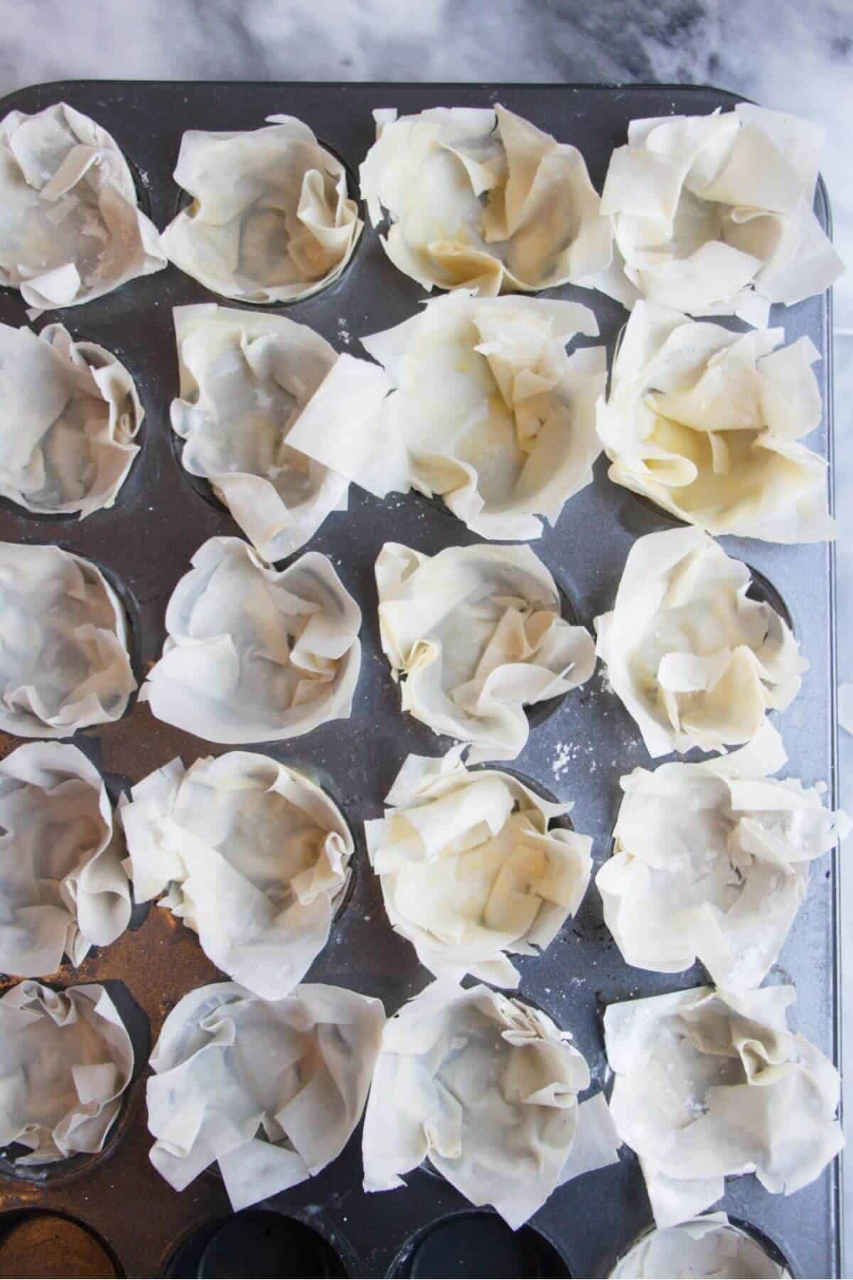 Squares of filo pastry pressed into s mini muffin tin.
