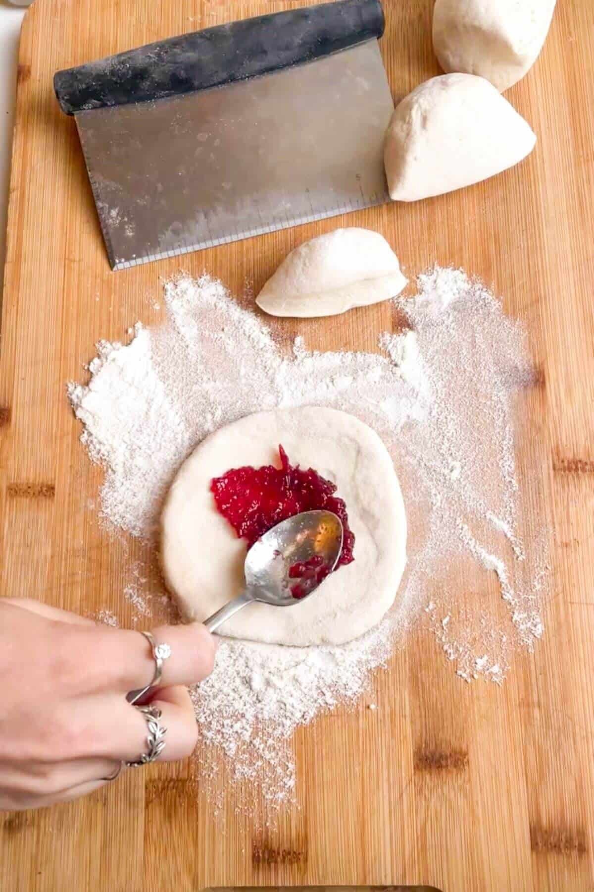 Spooning cranberry sauce in the middle of a piece of dough on a wooden board.