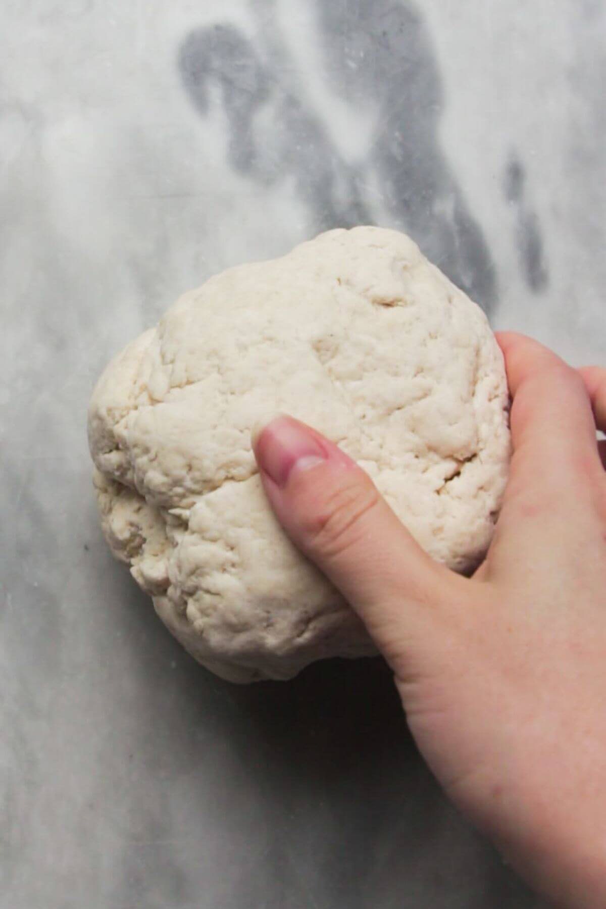 Hand placing dough on a grey marble countertop.