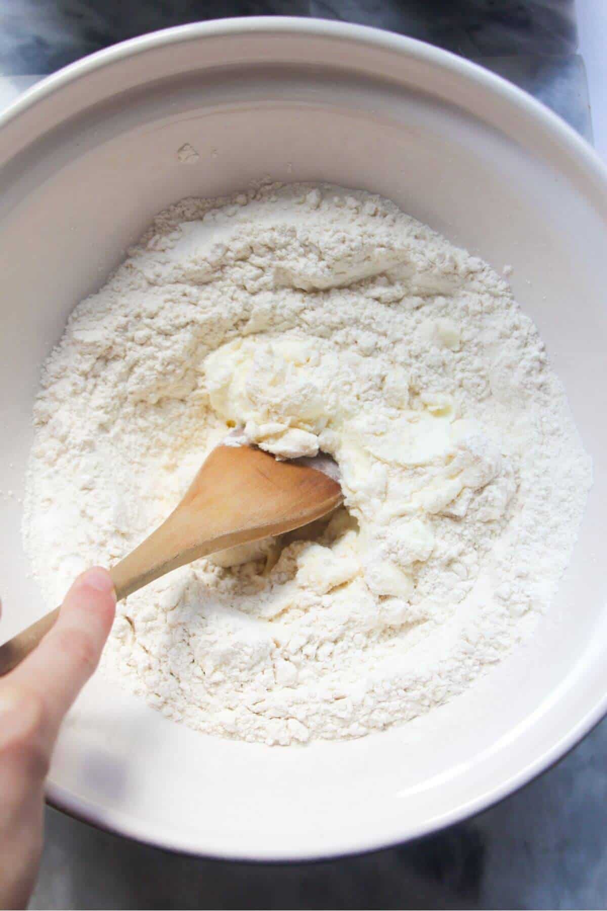 Flour and yogurt in a large white ceramic bowl about to be mixed with a large wooden spoon.