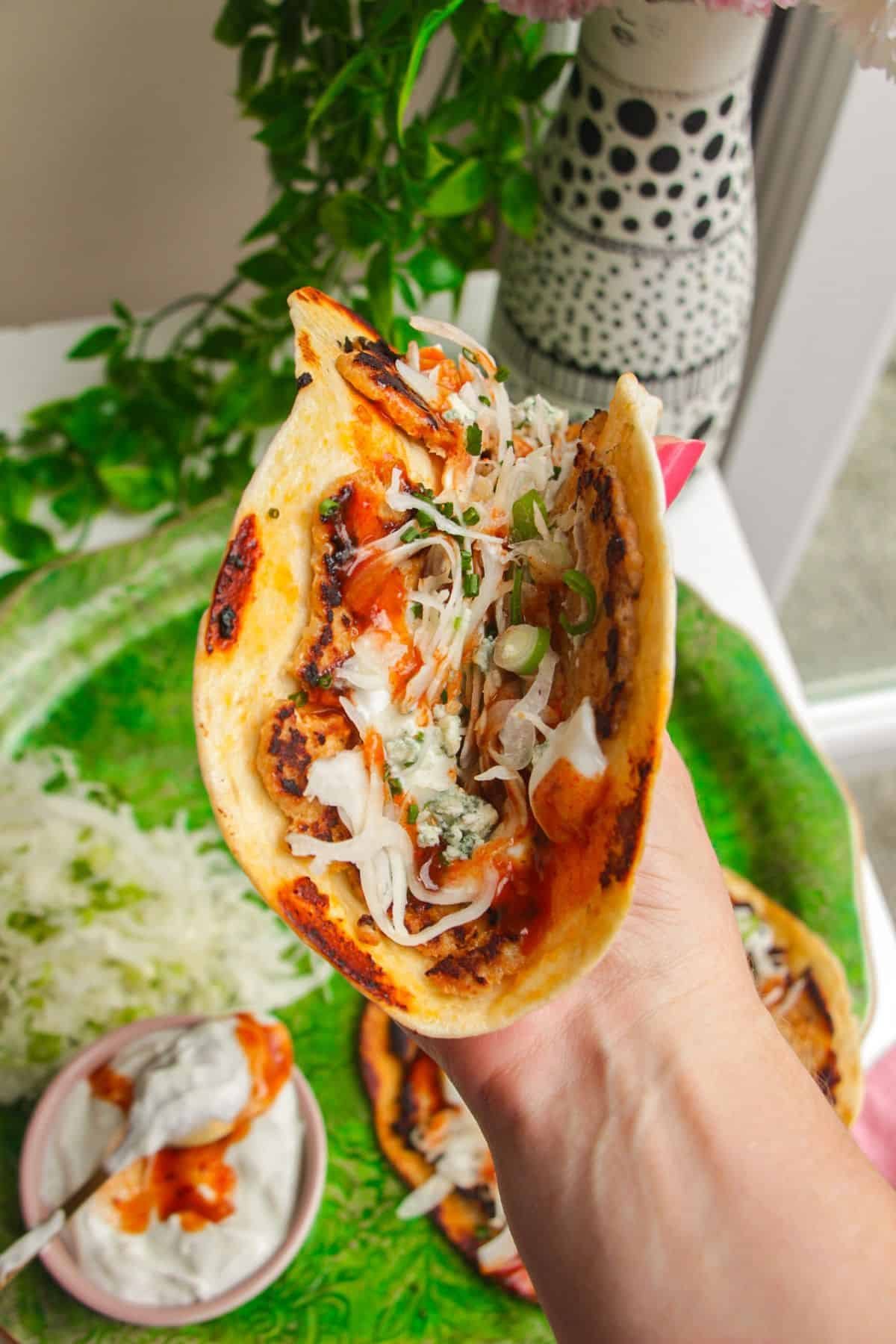 Holding a buffalo chicken taco with more in the background.