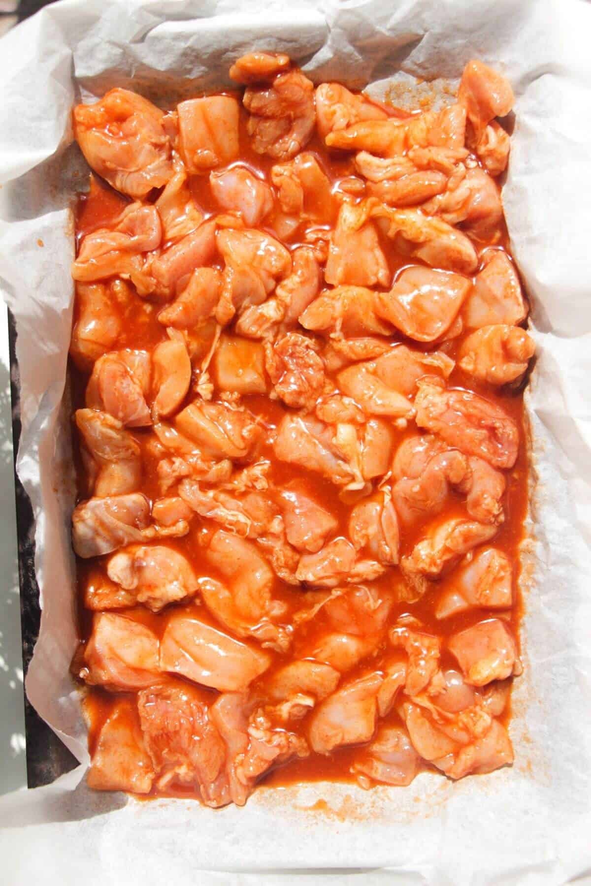 Buffalo marinated chicken thigh pieces on a lined oven tray.