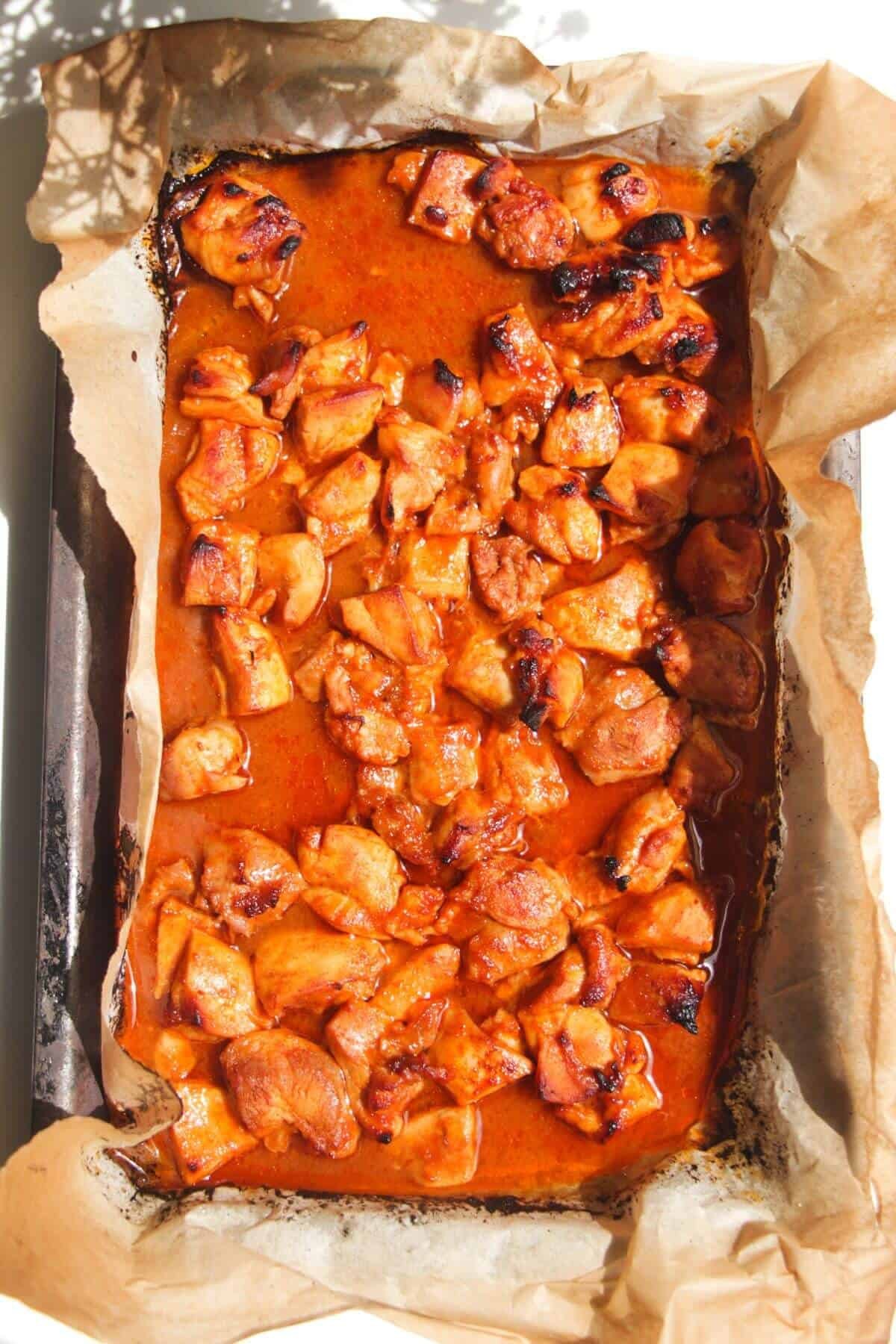 Cooked Buffalo chicken pieces on a lined oven tray.