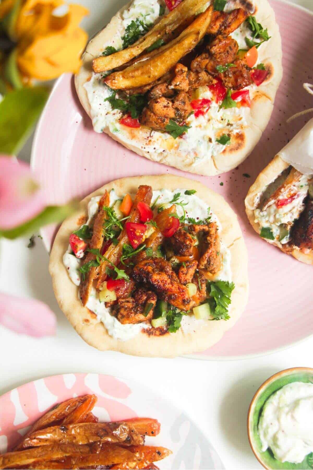 Three chicken gyros flatbreads on a pink plate.