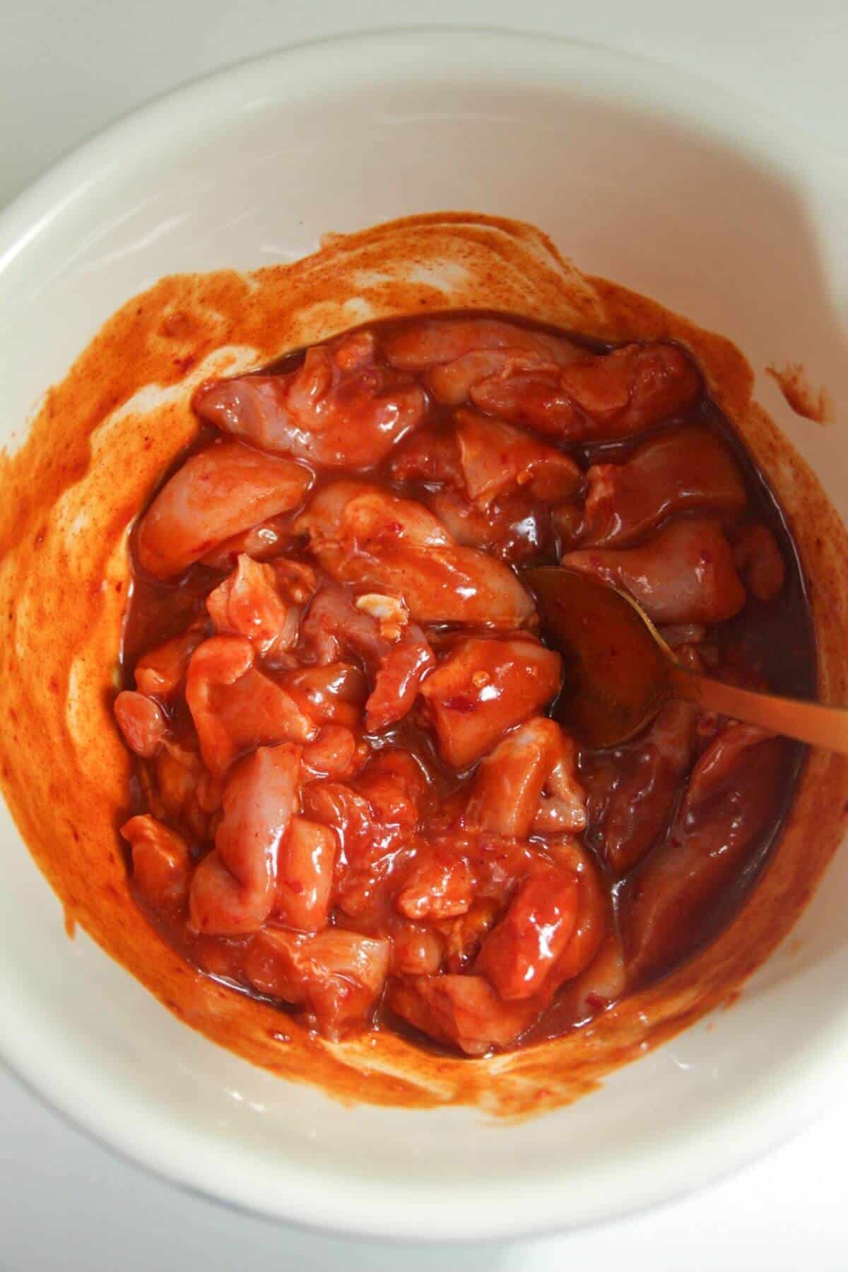 Mixing Buffalo marinade with chicken thigh pieces.