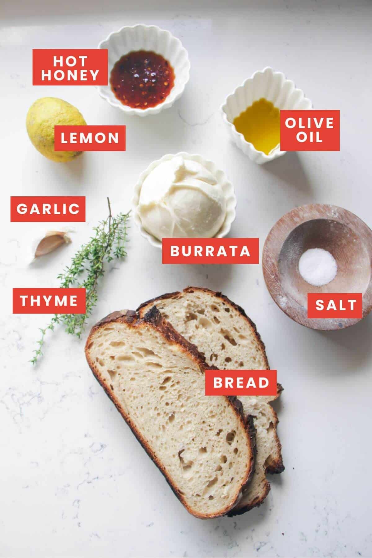 Ingredients for burrata toast with hot honey laid out on a white marble background and labelled.
