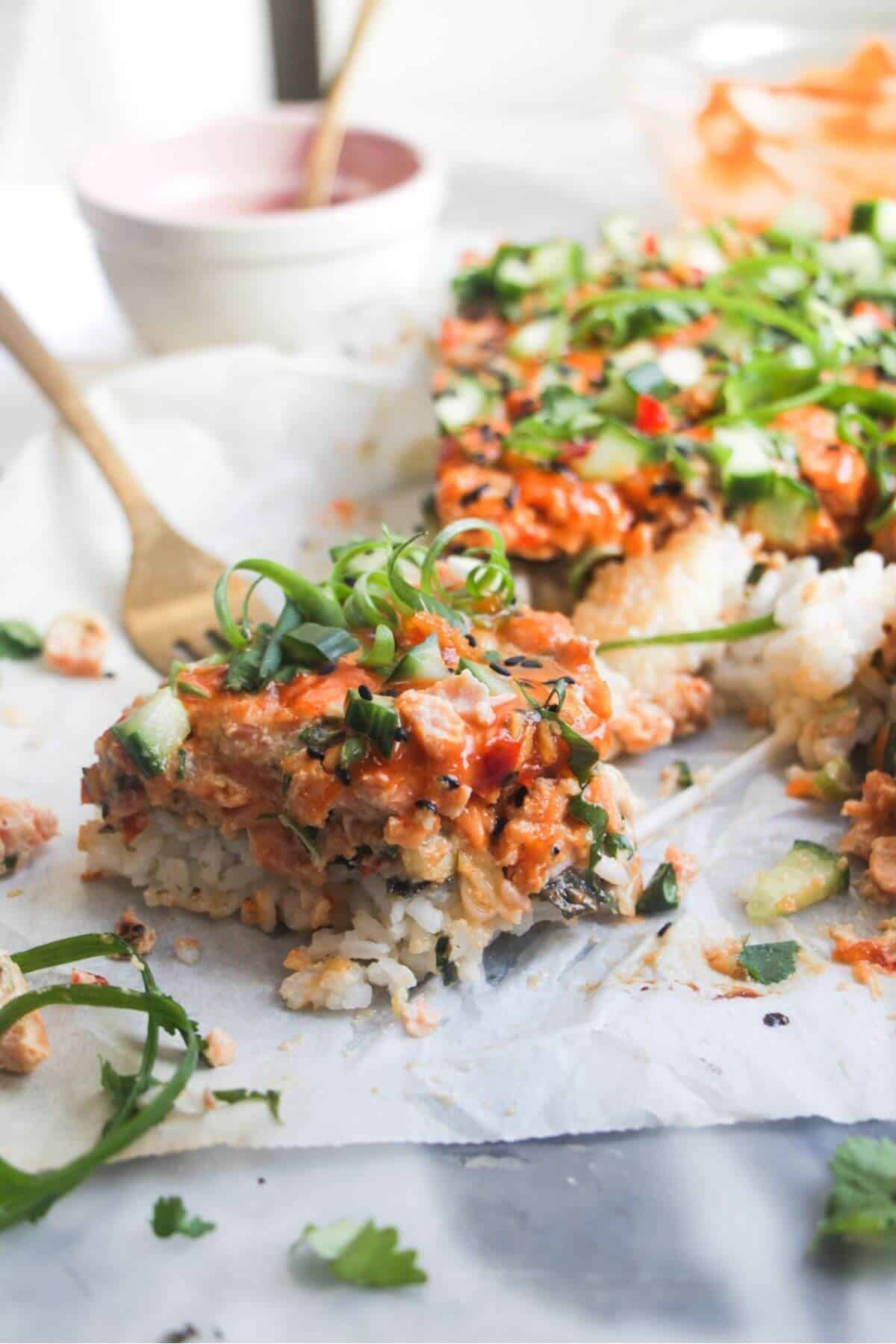 Close up of a piece of salmon sushi bake, with the rest of the bake in the background.