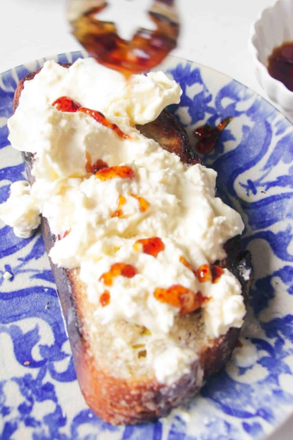 Spoon drizzling hot honey over torn burrata on a piece of toasted sourdough.