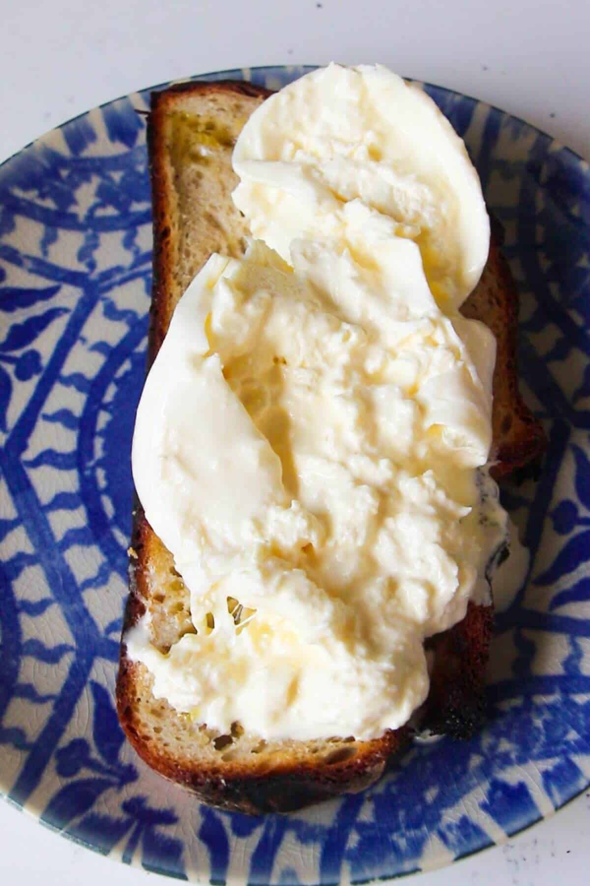 Torn burrata on a piece of toasted sourdough on a blue and white patterned plate.