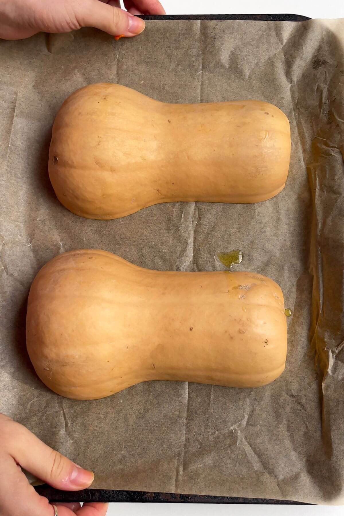 Halved squash upside down on a lined baking tray.