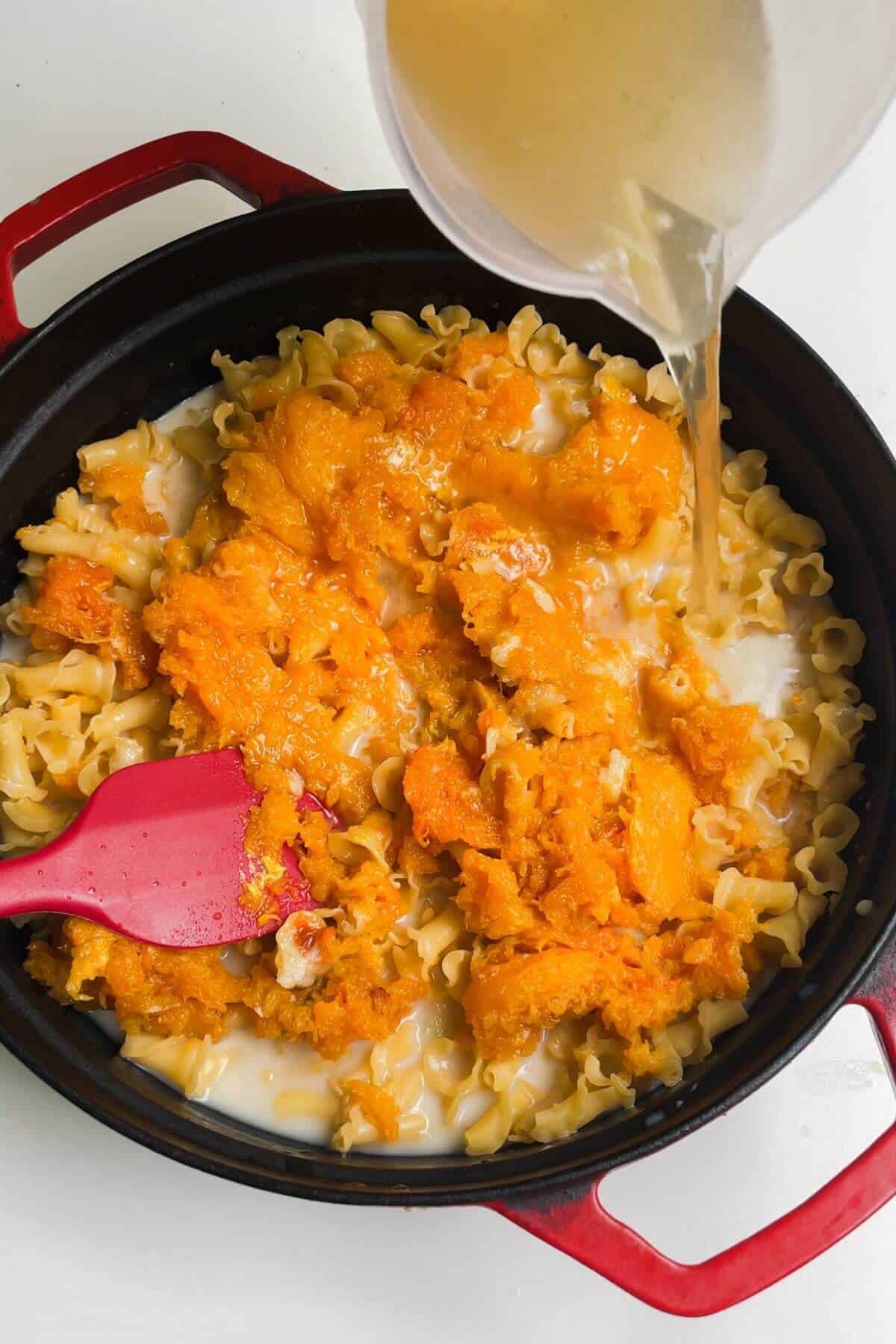 Stock being poured into skillet with pasta and butternut squash.