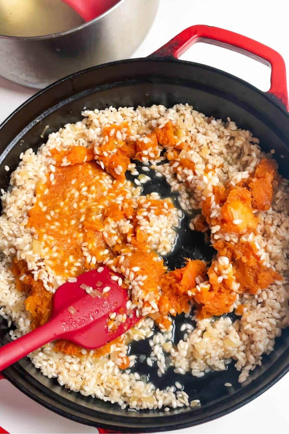 Roasted butternut squash added to rice in a pan.