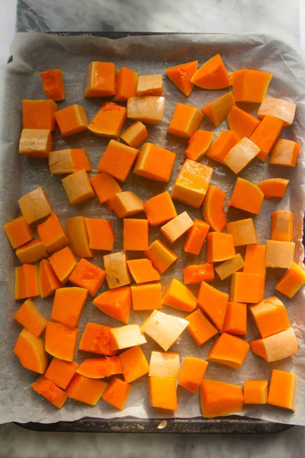 Butternut squash cubes on a lined oven tray.