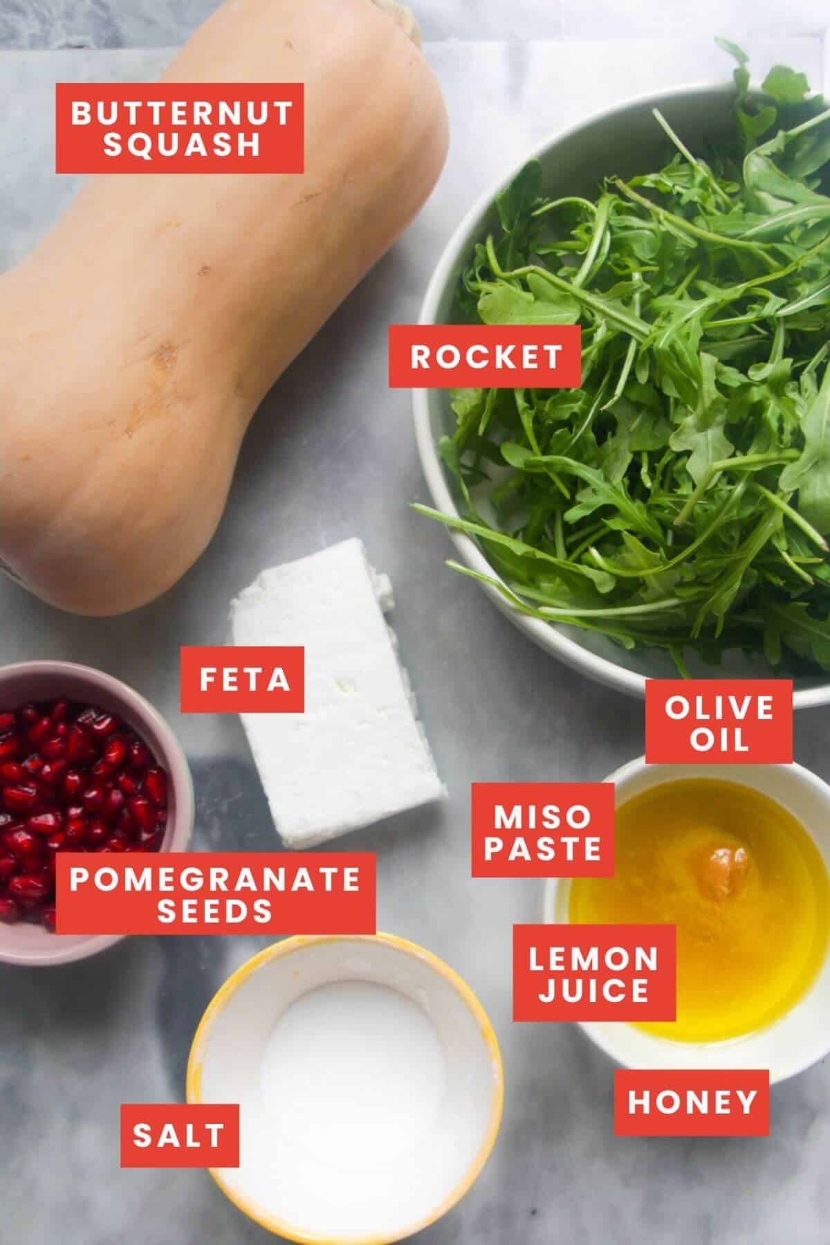 Ingredients for butternut squash salad laid out on a grey marble background and labelled.