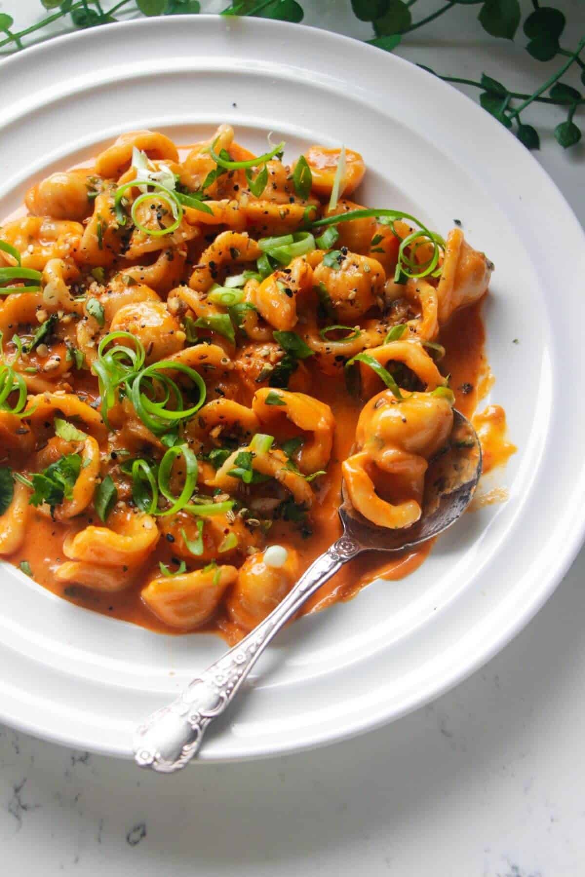 Close up of gochujang pasta on a white plate with a silver spoon in it.