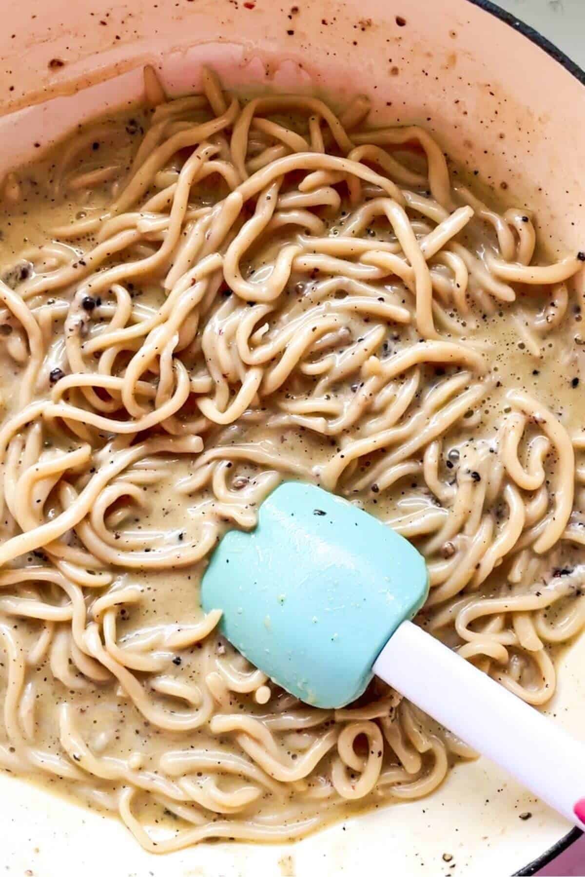 Spatula tossing pasta through cheesy cacio e pepe in a pan.