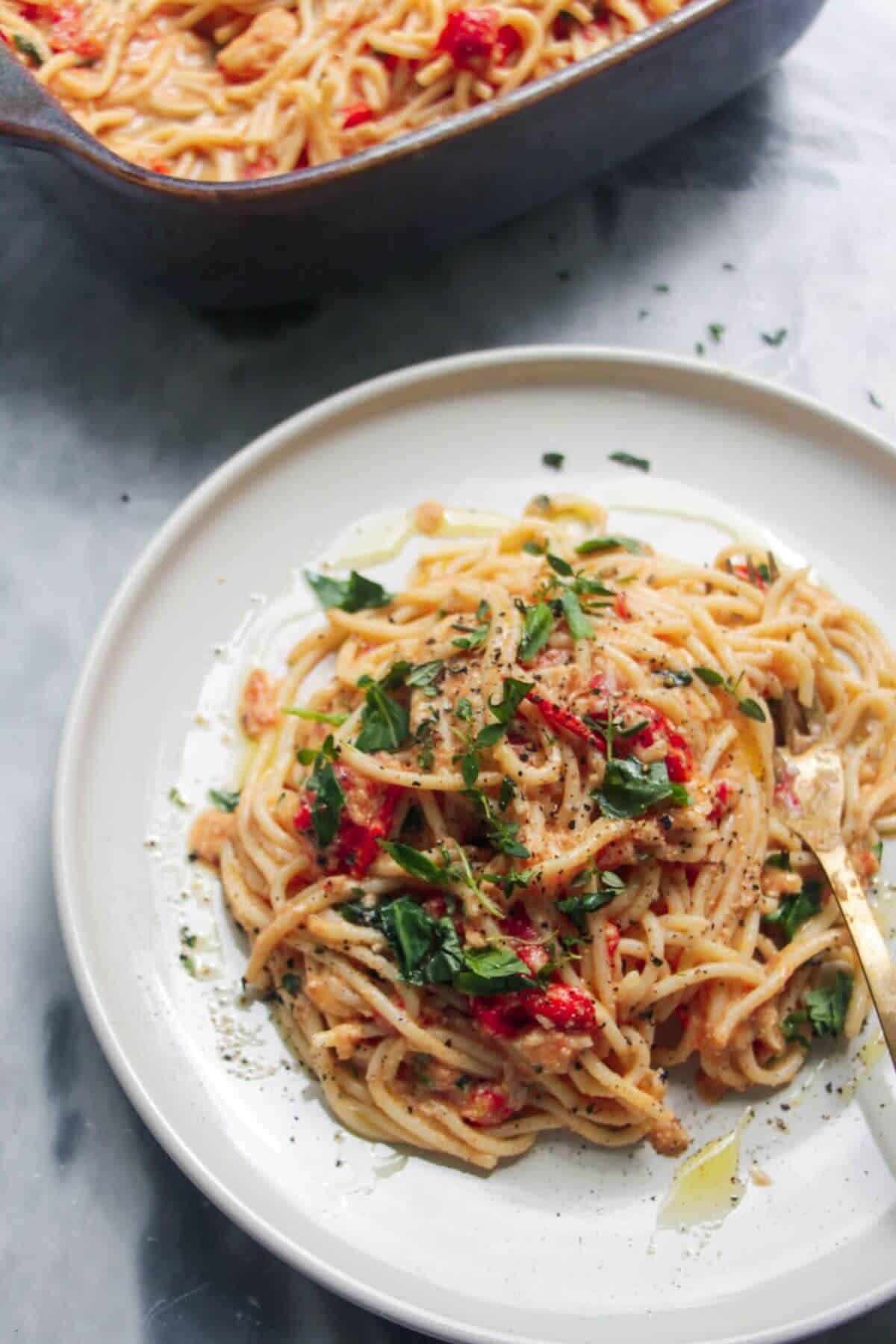 Baked tomato and burrata pasta on a white plate, with blue dish of pasta in the background.