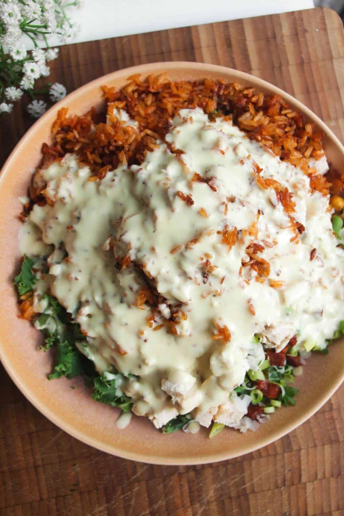 Caesar dressing poured over crispy rice salad in pink bowl.