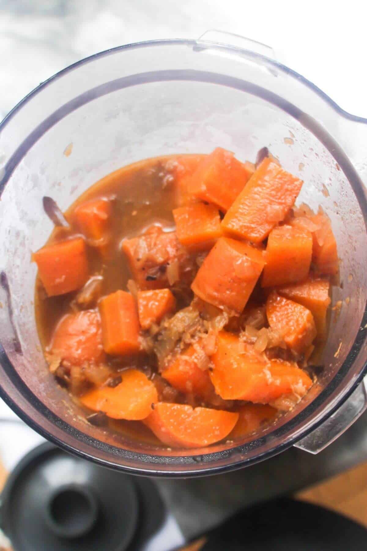 Softened carrot chunks, spices and stock in a blender a bout to be blended up.