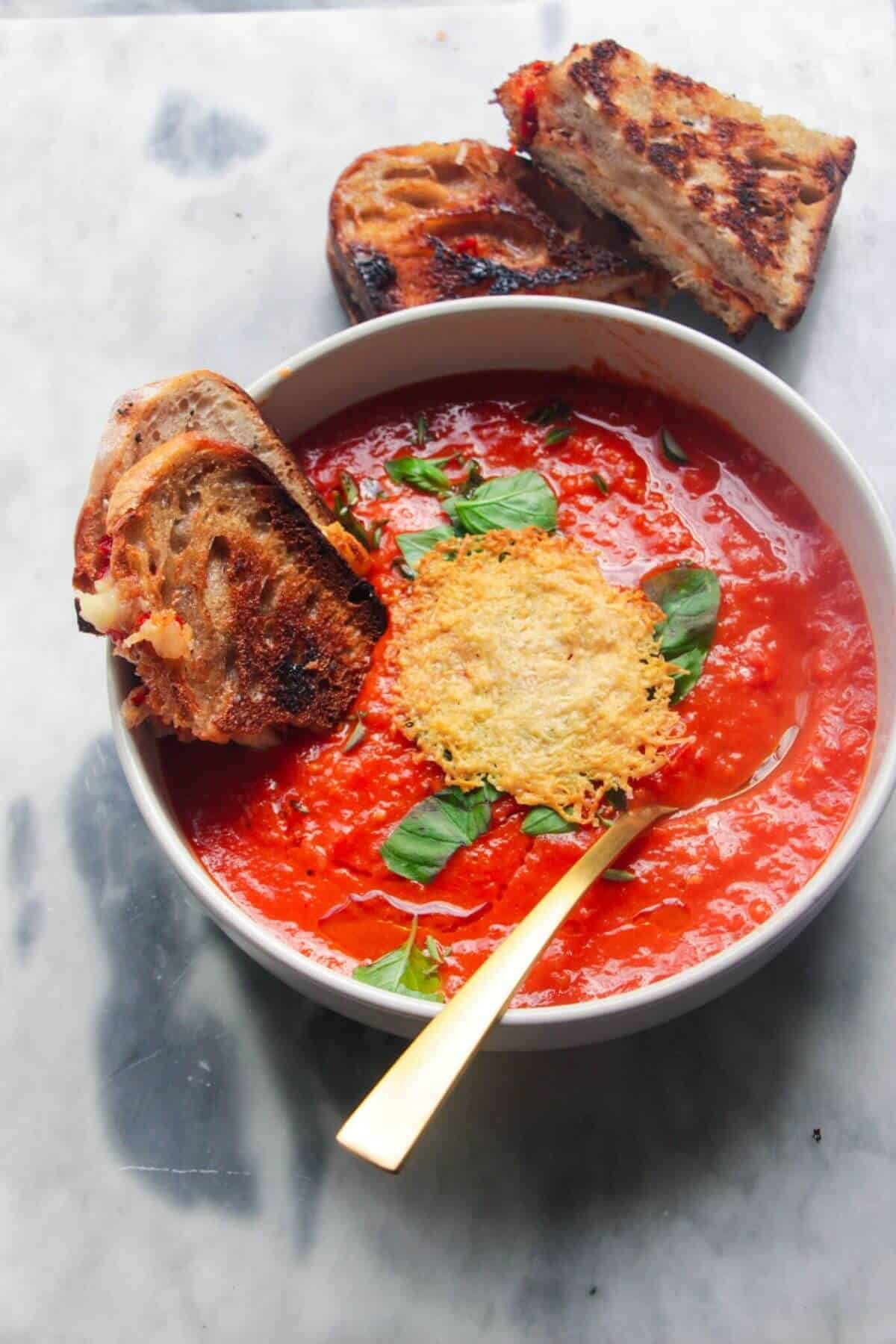 Roasted red pepper and tomato soup in a white bowl with grilled cheese dipped in.