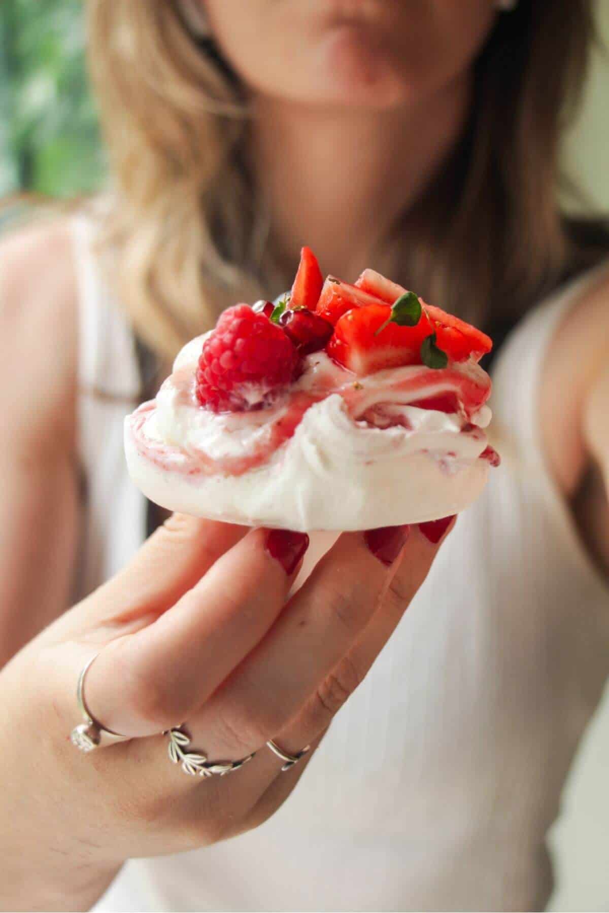 Holding up a mini pavlova topped with cheesecake cream and berries.