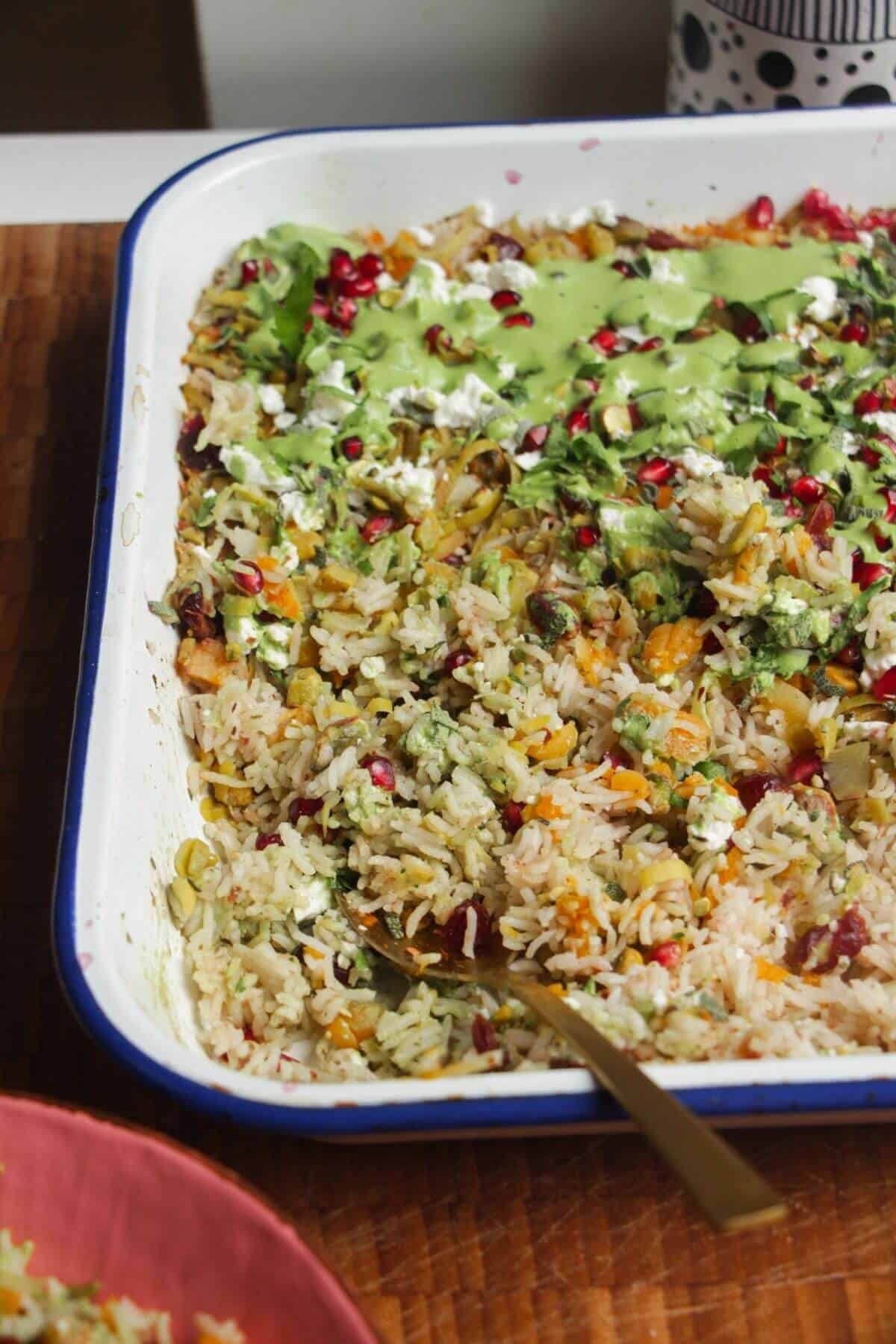Spoon in baked rice topped with feta, pomegranate seeds and green tahini sauce.