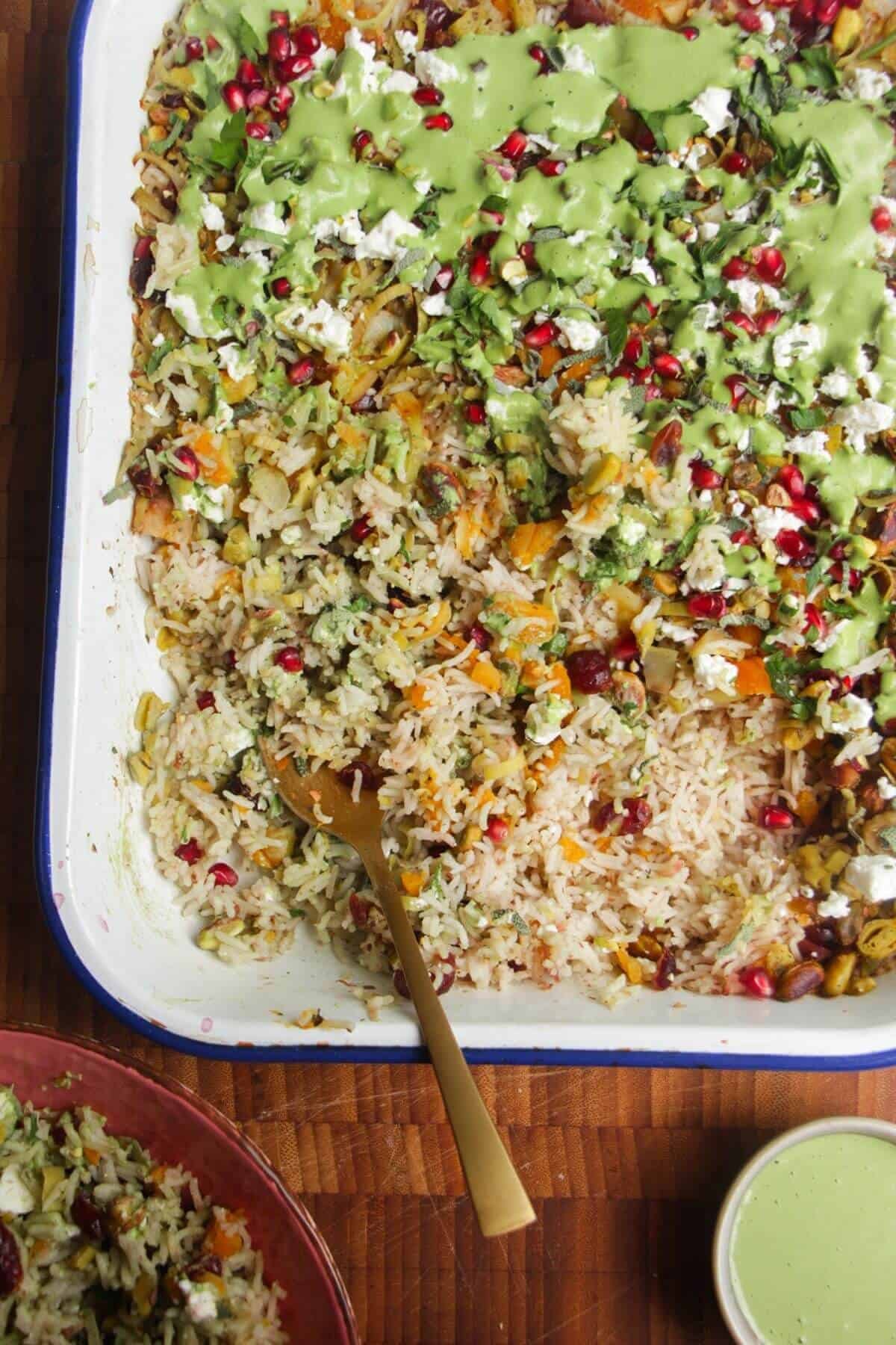 Spoon in baked rice topped with feta, pomegranate seeds and green tahini sauce.